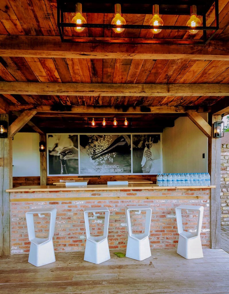 Rustieke bar met bakstenen muur, houten balken en industriële lampen in Feestlocatie Alegria