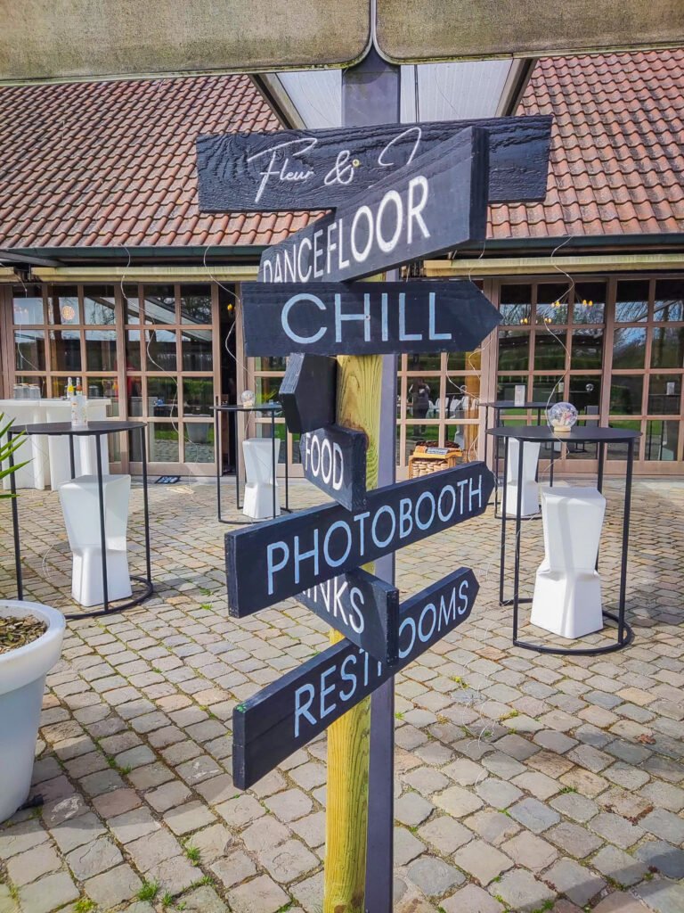 Wegwijzerborden bij de ingang met aanduiding voor dancefloor, chill, food, photobooth, drinks en restrooms bij Feestlocatie Alegria